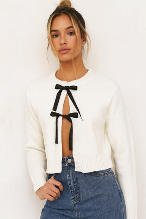 Cream knitted lace-up cardigan with black bow ties at center front, long sleeves