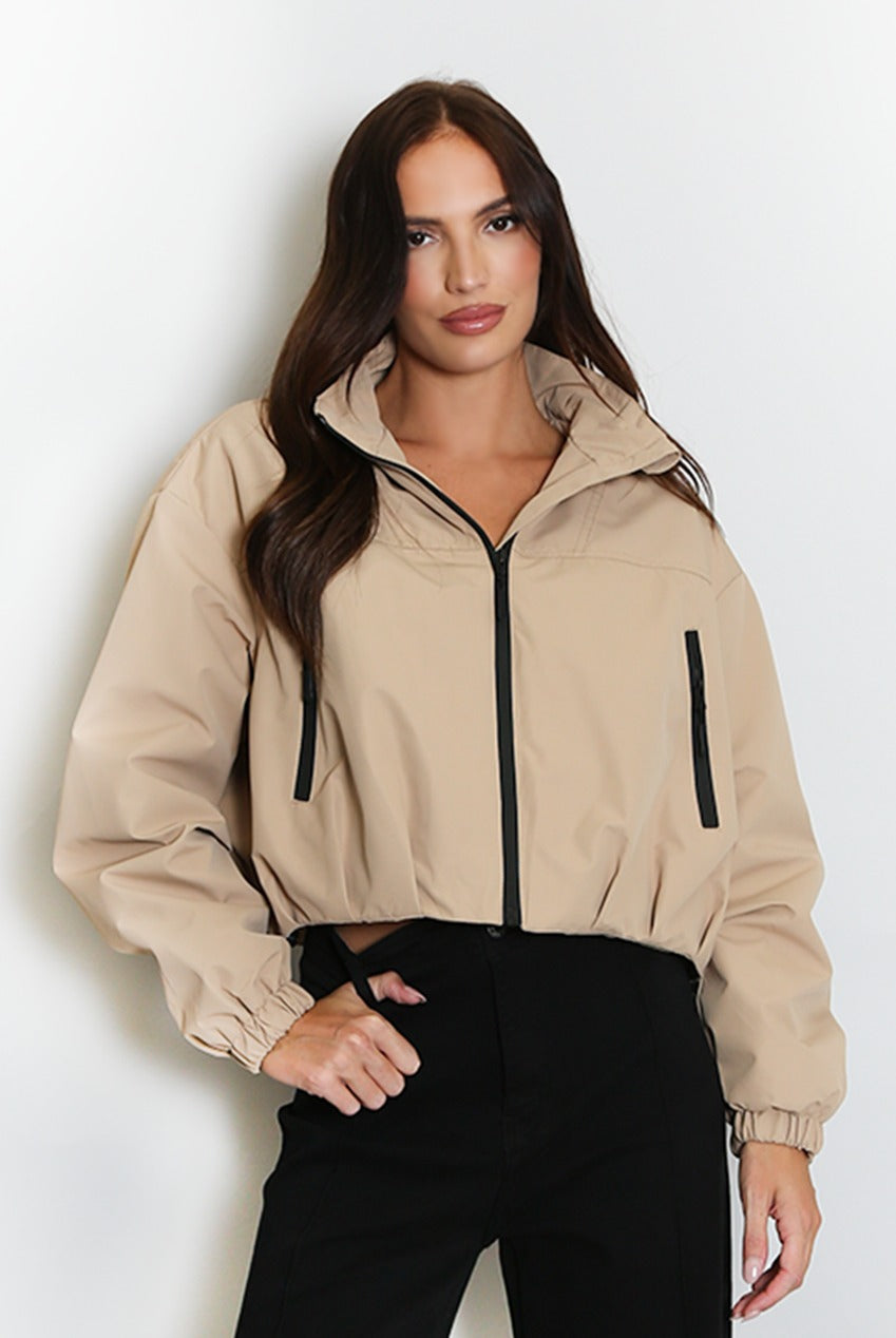 Beige cropped hooded jacket with black zipper, contrast hood lining, side stripe detail.