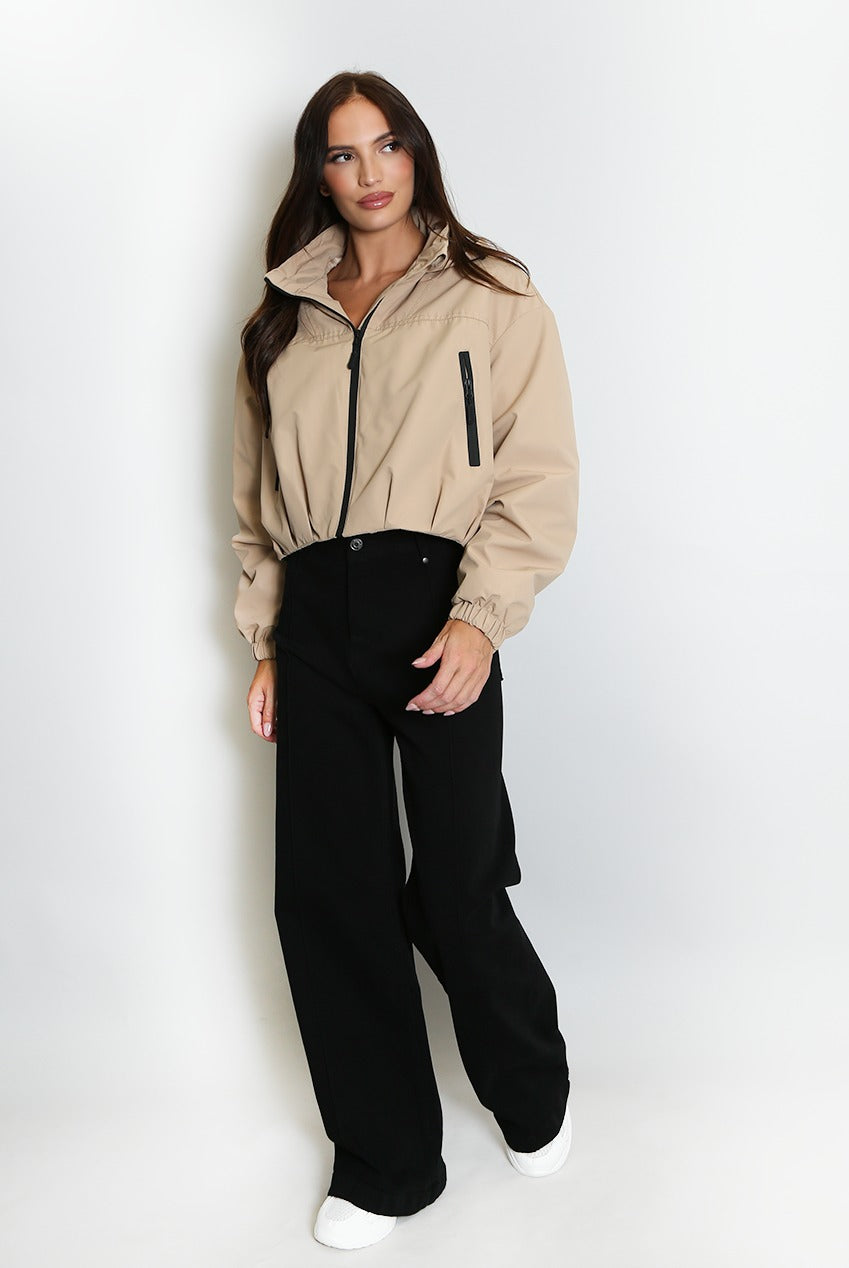 Beige cropped hooded jacket with black front zipper, contrast trim, ribbed cuffs.