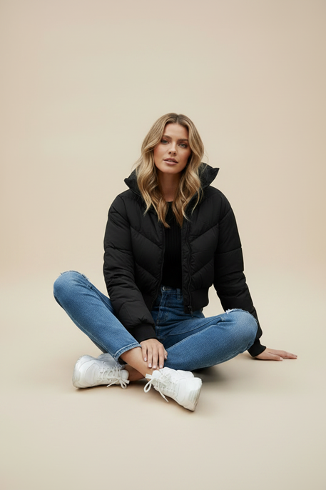 Black quilted puffer jacket with hood and front zipper; model wears blue jeans.
