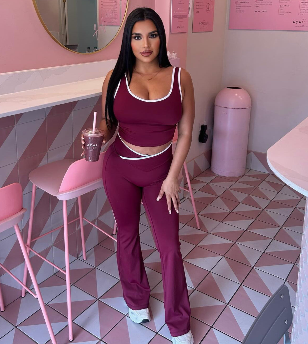 Woman in a maroon outfit holding a drink in a pink-themed room.